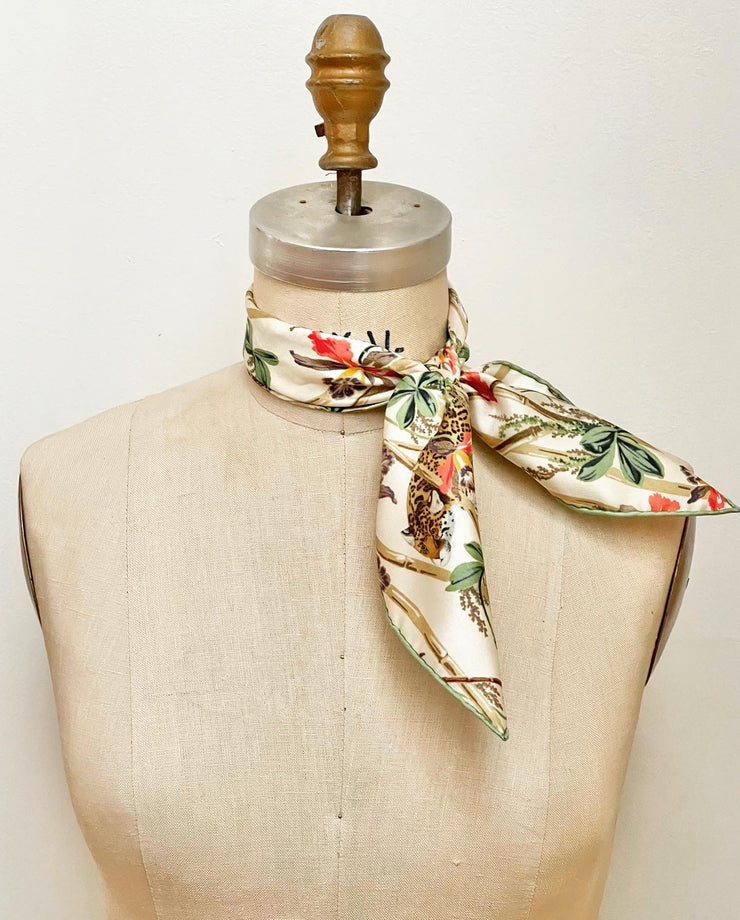 a luxury, bespoke Elwyn New York silk bandana tied on the neck of a form with a vintage tropical, floral, bamboo, leopard wall paper print