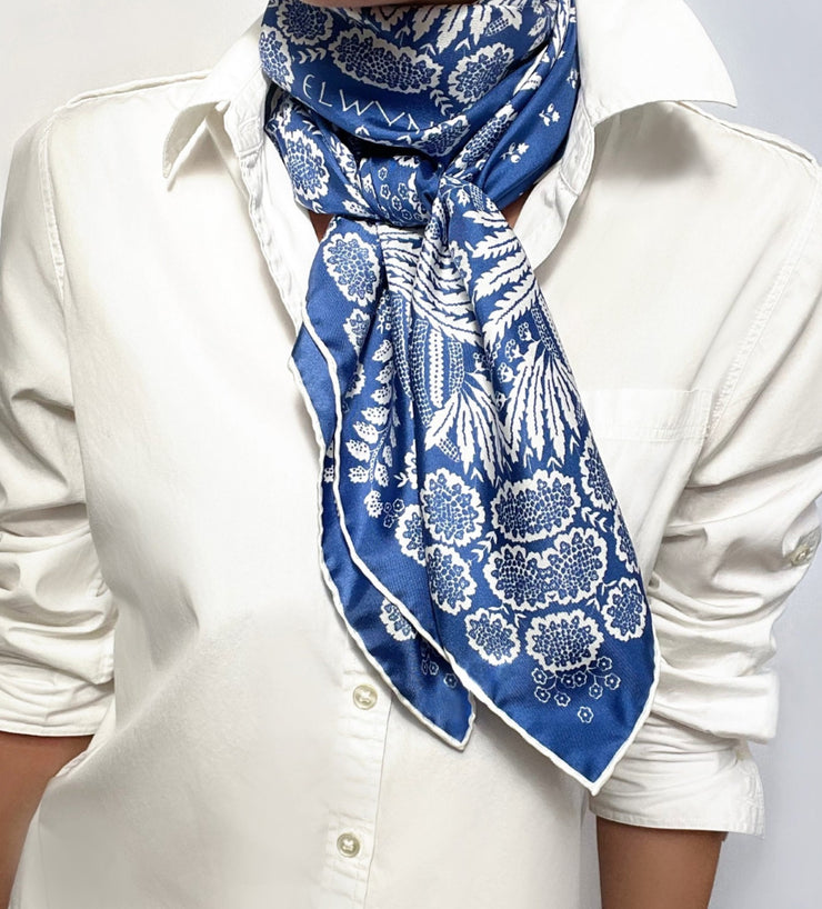 Woman wearing a bespoke Elwyn New York Scarf wrapped around her neck with an ornate, blue and white, vintage-pastoral bandana design. Classic, feminine, and romantic