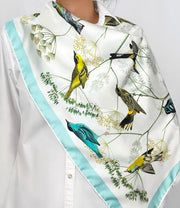 a classic woman wearing a personalized, bespoke Elwyn New York silk scarf draped around on her shoulders with a Charming blue and yellow warbler birds, flying and perched amidst delicate wild flowers. Inspired by nature found in the North East.