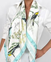 a classic woman wearing a personalized bespoke Elwyn New York silk scarf draped around her neck with a Charming blue and yellow warbler birds, flying and perched amidst delicate wild flowers. Inspired by nature found in the North East.