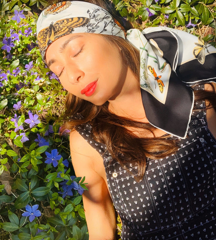 Classic woman, laying in a patch of wildflowers, wearing a luxury, bespoke Elwyn New York silk scarf draped on her head with a vintage style, botanical, floral, butterfly and leopard print