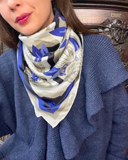 Front view of a classic woman wearing a cozy blue sweater and a bespoke, luxury elwyn new york silk scarf looped around her neck. This Denim friendly, zig-zag, art deco floral print feels modern and graphic.