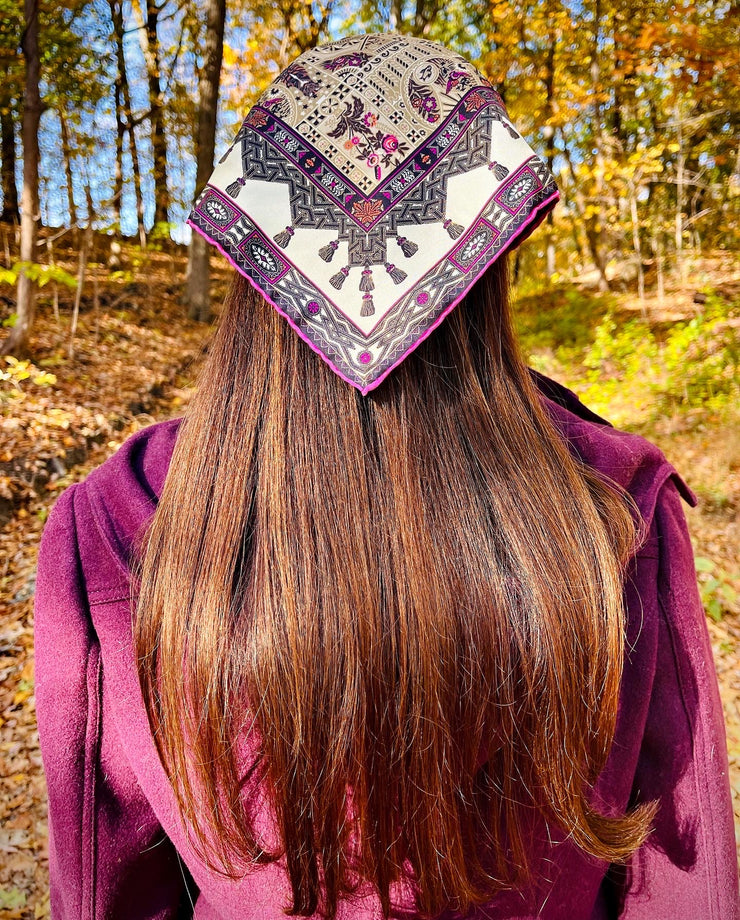 A model walking in the fall foliage wearing an Italian silk bandana with a geometric print on her head.  Like a head scarf . 