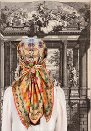 An Italian silk scarf featuring a geometric design, mixing earth tones and pops of brightly colored etymological butterflies tied around the model's head. 