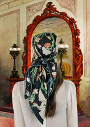 Fantasy Image: Back view of a classic woman wearing bespoke Elwyn New York Scarf tied on her head with a botanical crane print is collaged together from antique glass and pearl, beaded embroideries of yesteryear. Woman is standing in front of a grand, carved ornate Mirror in a mansion