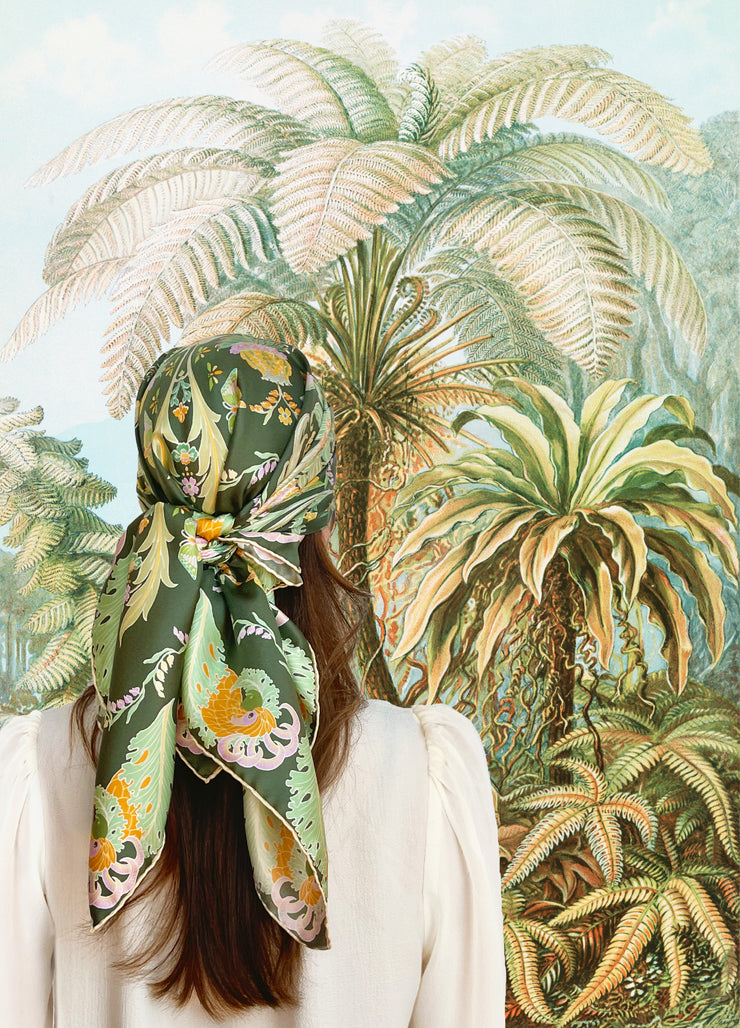 A classic model wearing an Italian silk scarf that is Art Nouveau inspired featuring a kaleidoscope of fantastical flowers, butterflies and cockatoos rising from the curling foliage tied around her head. 