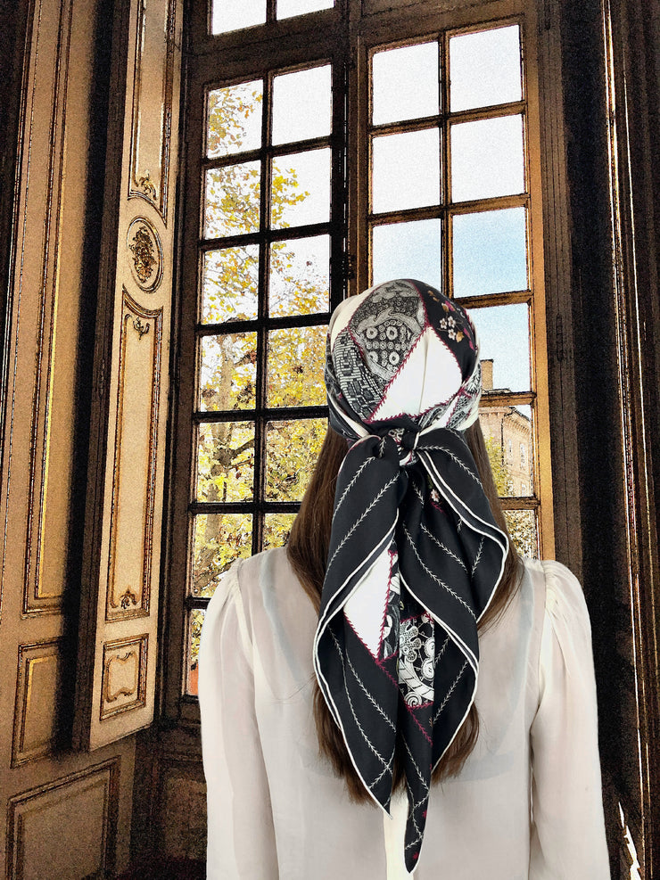 fantasy image: Back View of a classic woman wearing a bespoke, luxury Elwyn New York silk scarf. This geometric crazy quilt print is a vintage-modern depiction of the year 2020 filled with digital embroidery and lace of years past. Woman is standing in front of an ornate window looking out