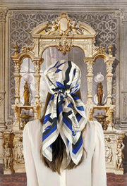 Fantasy image: Back view of a classic woman wearing a bespoke, luxury elwyn new york scarf on her head. This Denim friendly, zig-zag, art deco floral print feels modern and graphic. Woman standing in front of an illustrated floor to ceiling marble carved mirror