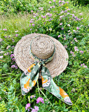 A hat wth an Italian silk scarf wrapped around the top with an Art Nouveau print inspired featuring a kaleidoscope of fantastical flowers, butterflies and cockatoos rising from the curling foliage