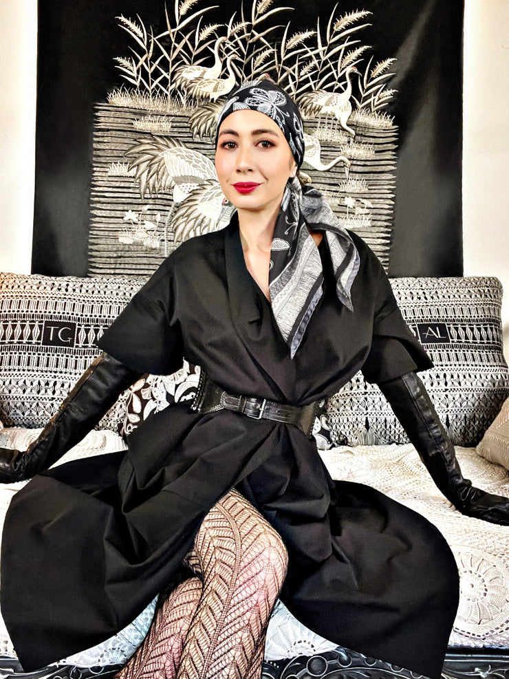 classic female wearing a belted black coat and bespoke, luxury, black and white Elwyn New York silk scarf around her head with vintage lace print and graphic fringe border