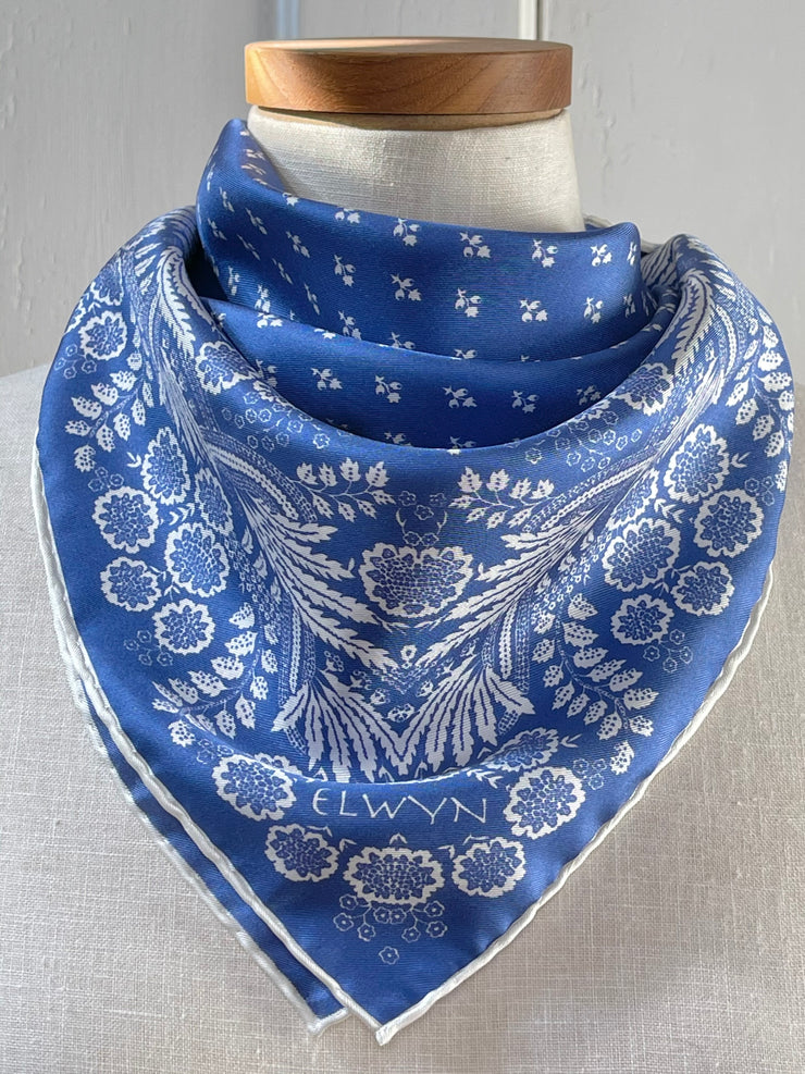 a closeup of a bespoke Elwyn New York bandana tied around the neck of a form like a bib with an ornate, blue and white, vintage-pastoral bandana design. Classic, feminine, and romantic.