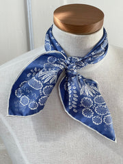 a closeup of a bespoke Elwyn New York bandana tied around the neck of a form with an ornate, blue and white, vintage-pastoral bandana design. Classic, feminine, and romantic.