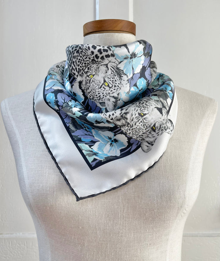 a bespoke Elwyn New York silk bandana, tied around the neck of a form like a bib with vintage style print of a bluish floral field and modern lazing leopards