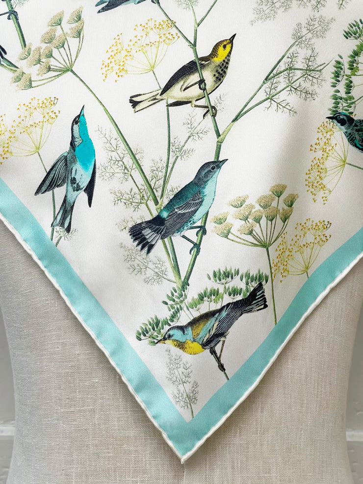 corner Closeup of a bespoke Elwyn New York silk bandana draped on the back of a form with a Charming blue and yellow warbler birds, flying and perched amidst delicate wild flowers. Inspired by nature found in the North East.