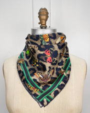 A designer silk bandana wrapped around the neck of a form. The Italian silk bandana Features a Leopard fur print, adorned with multicolored entomological moths, butterflies, beetles, and dragonflies and framed by a rope ribbon border. Imagined to be a sleeping Leopard, where butterflies and the such come to land and rest on her back in a daydream...  This is a hand sewn silk scarf.