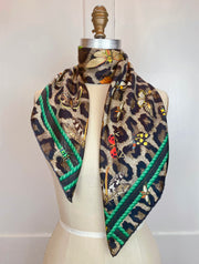 A designer silk scarf wrapped around the neck of a form.  The Italian silk scarf Features a Leopard fur print, adorned with multicolored entomological moths, butterflies, beetles, and dragonflies and framed by a rope ribbon border.  Imagined to be a sleeping Leopard, where butterflies and the such come to land and rest on her back in a daydream...   