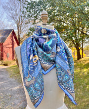  An Italian silk scarf with a wallpaper type print, featuring radiant peacocks, amidst sprigs of yellow poppies, surrounded by ornate ribbons folding around the border tied around a form. 