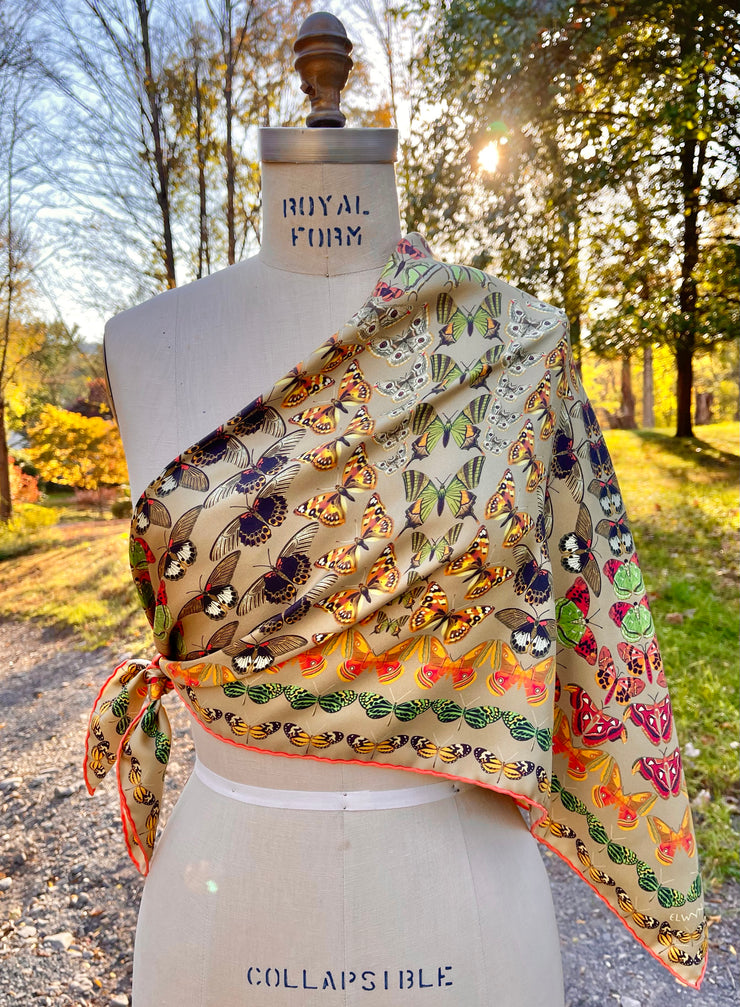 An Italian silk scarf featuring a geometric design, mixing earth tones and pops of brightly colored etymological butterflies tied around a dress form.