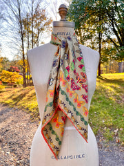 An Italian silk scarf featuring a geometric design, mixing earth tones and pops of brightly colored etymological butterflies tied around a dress form's neck.