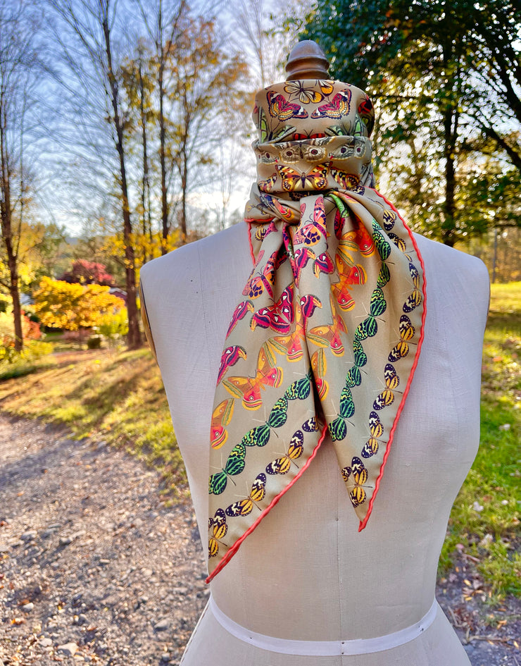An Italian silk scarf with a Geometric Design, mixing earth tones and pops of brightly colored etymological butterflies tied around the neck of a dress form. 