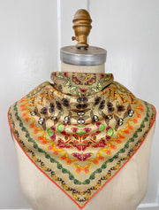 An Italian silk bandana featuring a geometric design, mixing earth tones and pops of brightly colored etymological butterflies tied around a mannequin's neck. 