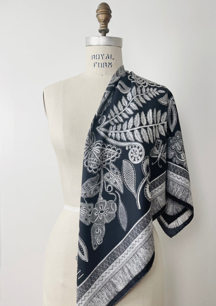 A bespoke, luxury, black and white Elwyn New York silk scarf draped on one shoulder of a form with a vintage lace print and graphic fringe border