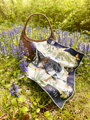 A luxury, bespoke Elwyn New York silk bandana spread across a wicker bag with a vintage style, botanical, floral, butterfly and leopard print