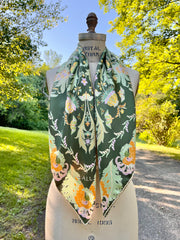 This bespoke, designer silk Scarf is Art Nouveau inspired featuring a kaleidoscope of fantastical flowers, butterflies and cockatoos rising from the curling foliage. The scarf is hanging around the neck of a form in the woods.
