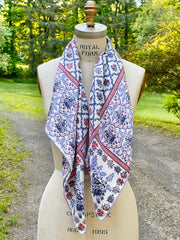 A dress form with a silk scarf around the neck. The main pattern is made up of a red, white and blue diamond lattice of curving ribbons, enclosing sprays of flowers and is surrounded by an eyelet lace border, adorned with charming little birds.