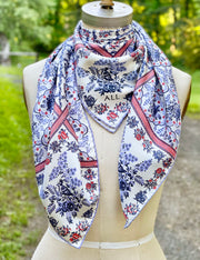 A dress form with a silk scarf tied around the neck. The main pattern is made up of a red, white and blue diamond lattice of curving ribbons, enclosing sprays of flowers and is surrounded by an eyelet lace border, adorned with charming little birds.
