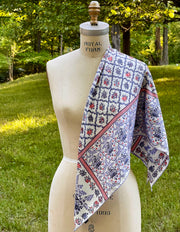 A silk scarf draped across a dress form's shoulder. The main pattern is made up of a red, white and blue diamond lattice of curving ribbons, enclosing sprays of flowers and is surrounded by an eyelet lace border, adorned with charming little birds.