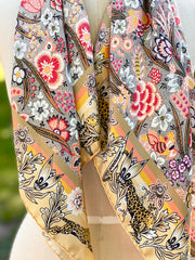 A dress form with a silk scarf around the neck that is rich with sunset colored wildflowers and energized leopards romping around the border. 