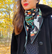 Classic woman standing outside amongst the autumn leaves, wearing bespoke Elwyn New York Scarf draped in a loop around her neck with a botanical crane print is collaged together from antique glass and pearl, beaded embroideries of yesteryear.
