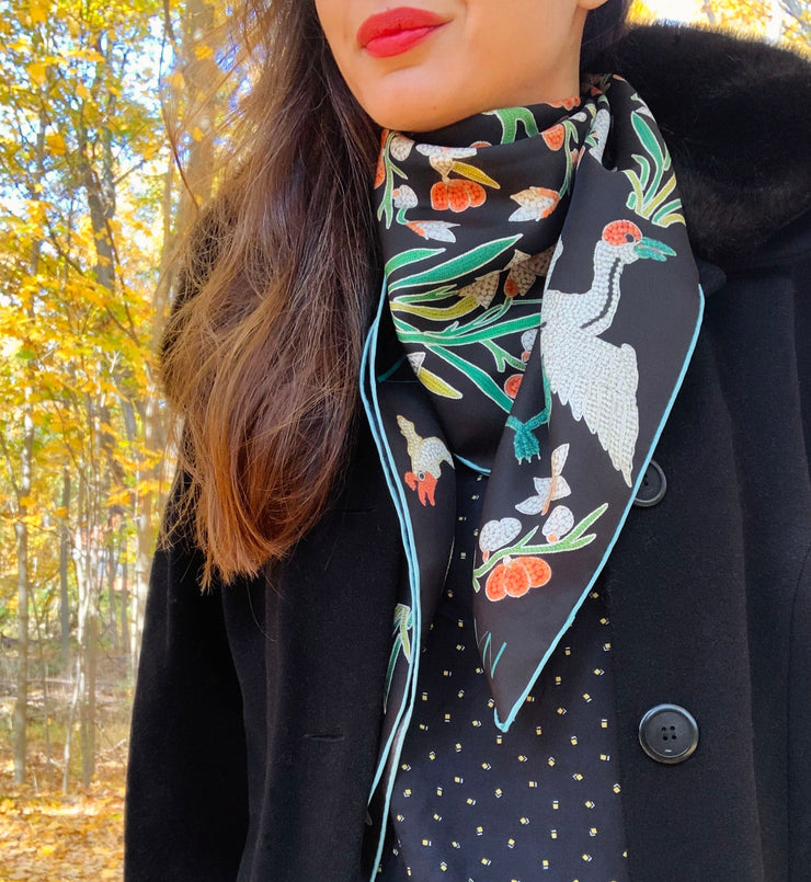 Classic woman standing outside amongst the autumn leaves, wearing bespoke Elwyn New York Scarf draped in a loop around her neck with a botanical crane print is collaged together from antique glass and pearl, beaded embroideries of yesteryear.