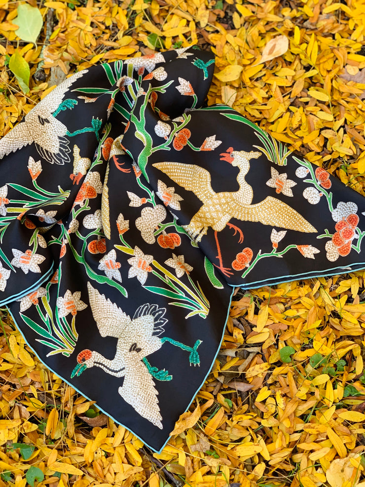 Image of a botanical crane and floral scarf laying in a bed of autumnal yellow leaves. the print is collaged together from antique glass and pearl, beaded embroideries of yesteryear.