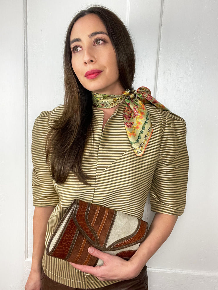 A model wearing a striped top, clutch, and Italian silk bandana with a geometric butterfly print tied around her neck. 