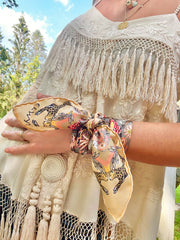 This Italian silk bandana is rich with sunset colored wildflowers and energized leopards romping around the border is tied around a classic model's wrist.