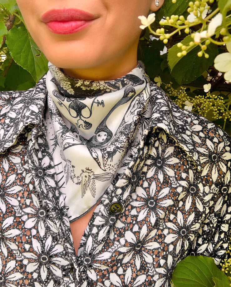 classic woman wearing an Elwyn New York luxury, bespoke Elwyn New York silk bandana with black and white, art nouveau, whimsical, storybook print. She is standing amongst blooming hydrangeas
