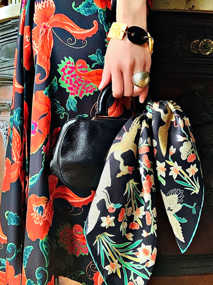 model holding a  little leather handbag with an Elwyn New York Italian silk bandana tied around the handle .  The print is collaged together from a variety of archival antique coral and pearl beaded embroideries of yesteryear.