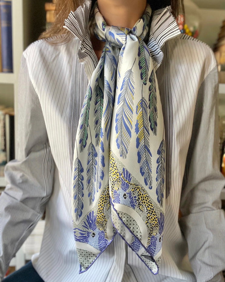 Woman wearing a bespoke Elwyn New York silk scarf knotted at her neck, with a delightful design of swirling feathers, surrounded by creeping jaguars and parrots in the graphic border.