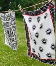 luxury, bespoke Elwyn New York silk bandana with black and white, whimsical, polka dot, bird and stars, storybook print hanging on a laundry line in the middle of a field