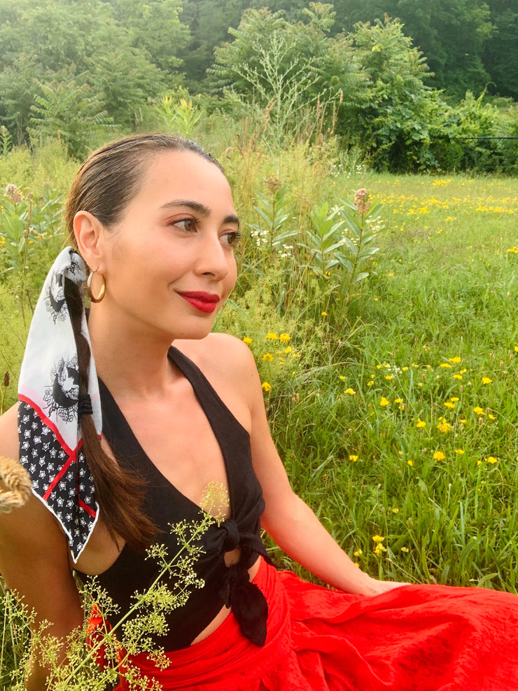 Classic woman sitting in a field wearing a luxury, bespoke Elwyn New York silk bandana in her hairwith black and white, whimsical, polka dot, bird and stars, storybook print