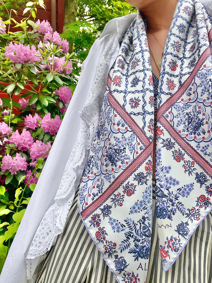 A classic model with a silk scarf around her neck. The main pattern is made up of a red, white and blue diamond lattice of curving ribbons, enclosing sprays of flowers and is surrounded by an eyelet lace border, adorned with charming little birds.