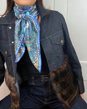 close up of a model wearing jeans , a faux fur jean Jacket and an Italian silk scarf with a Peacock and paisley print around her neck . 