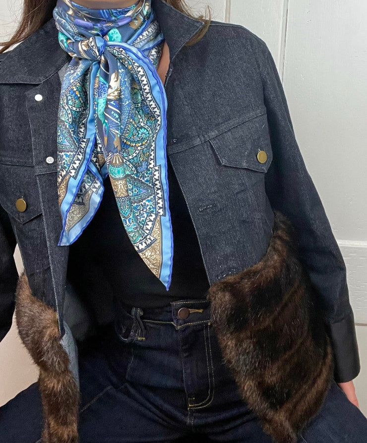 Close up of a  model wearing jeans , a faux fur jean Jacket and an Italian silk scarf with a Peacock and paisley print around her neck . 