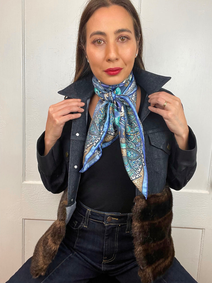 A model wearing jeans , a faux fur jean Jacket and an Italian silk scarf with a Peacock and paisley print around her neck . 