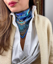 A model wearing a button up shirt and an Italian silk bandana with a Peacock and paisley print around her neck . 