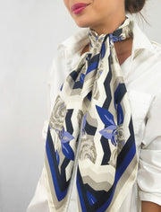 A classic woman wearing a bespoke, luxury elwyn new york scarf draped loose and long around her neck. This Denim friendly, zig-zag, art deco floral print feels modern and graphic.