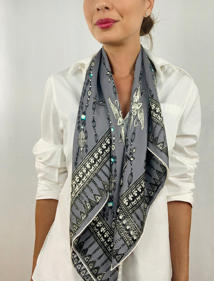 Classic woman wearing a bespoke Elwyn New York silk scarf loose and long around her neck with a vintage chain and beaded sautoir print that has intricate, little charm motifs that are strung together in long flowing chains.
