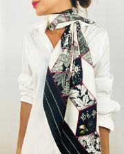 Classic woman wearing bespoke, luxury Elwyn New York silk scarf draped long and loose around her neck. This geometric crazy quilt print is a vintage-modern depiction of the year 2020 filled with digital embroidery and lace of years past. One can see the words LGBTQ and BLM depicted in this photo